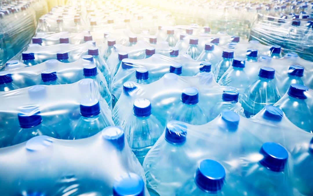 Stacks of large bottled water with blue caps, wrapped for delivery, are grouped in a clean, well-lit space.
