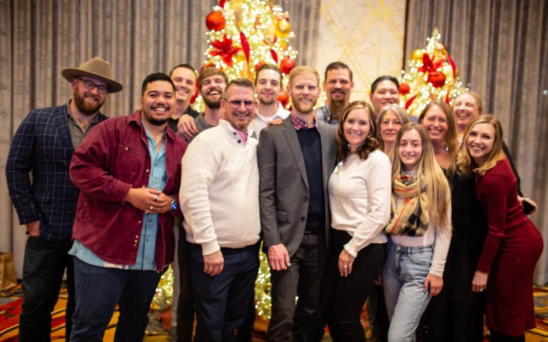 Smiling team poses together in front of decorated Christmas trees at a Clean Water Co. indoor location.