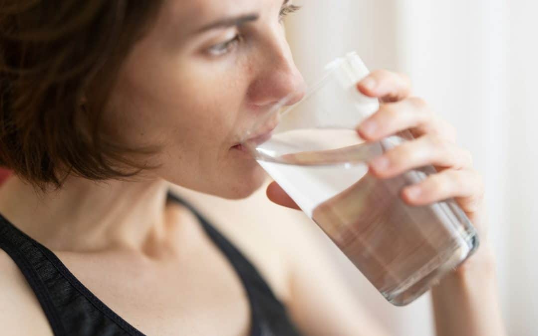 A person with short brown hair enjoys a glass of Clean Water Co. filtered water, promoting healthy hydration.