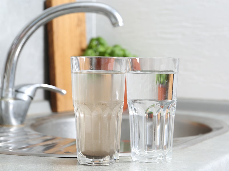 denver-well-water-testing Two glasses—one cloudy, one clear—sit on a kitchen counter, illustrating the benefits of Clean Water Co. filtration.