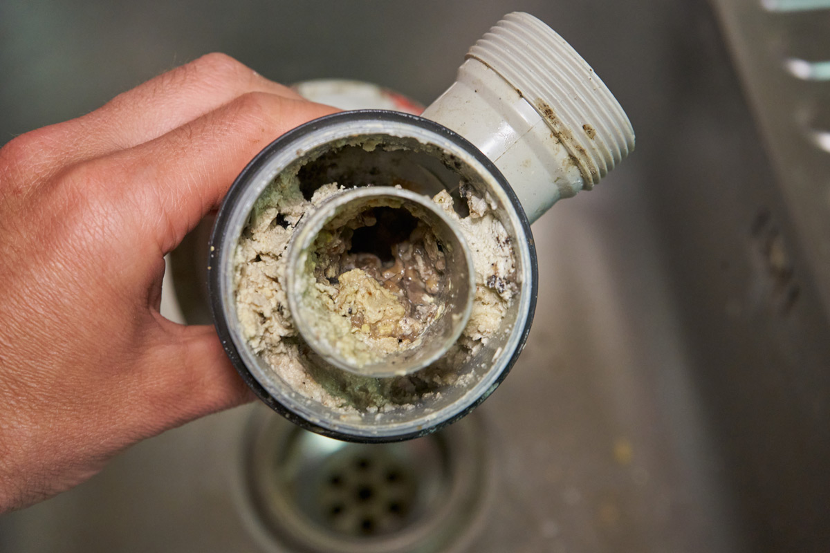clogged-drain-pipe A hand holds a clogged, debris-filled pipe over a sink drain—a reminder to keep your Colorado Springs water system clean.