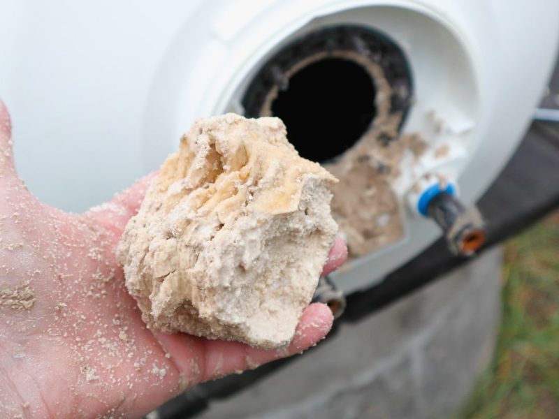 A hand displays mineral buildup taken from a water heater, highlighting the impact of hard water on home plumbing systems.